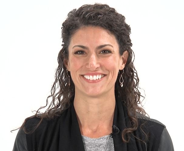 A smiling person with curly hair wears a gray shirt and black jacket, possibly using medbridge software.