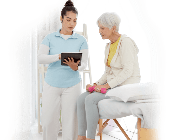 A healthcare worker shows digital info on a tablet to an older woman with pink dumbbells, seated on a treatment table, using medbridge.
