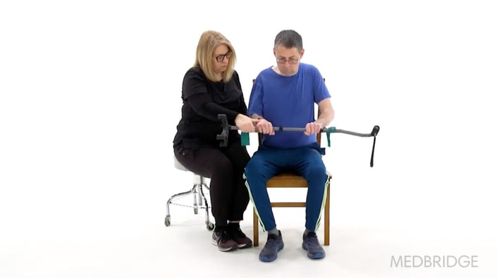 A woman helps a man use a leg exercise device while demonstrating healthcare training with medbridge software.