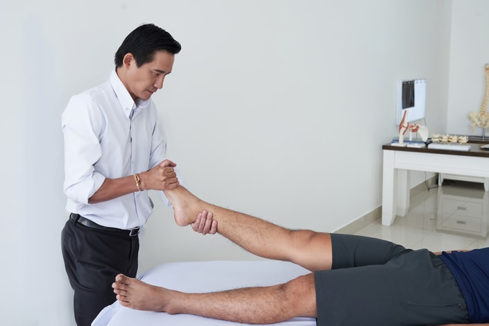 A therapist in a white shirt examines a patient's leg using digital healthcare tools from Medbridge.