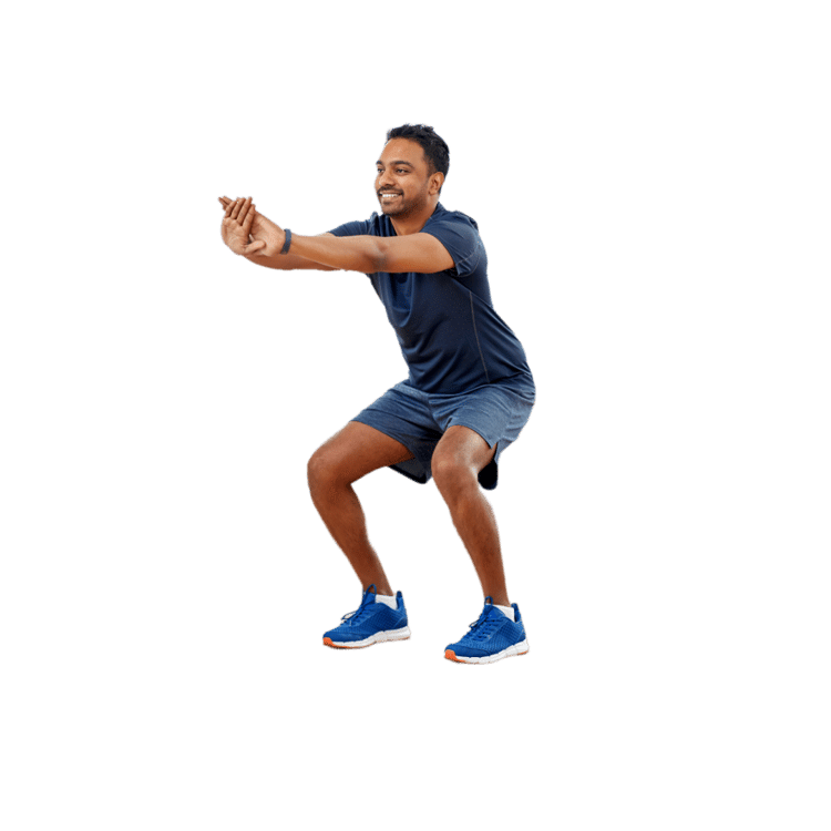 A man in a dark blue outfit and athletic shoes is smiling while squatting with clasped hands against a white backdrop.