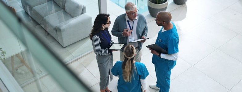 Four healthcare professionals review information on tablets and clipboards with medbridge patient care software indoors.