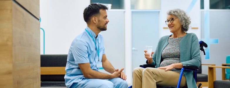 A healthcare worker in scrubs talks with an older woman in a wheelchair at a facility using medbridge patient care software.
