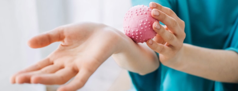 A person in a teal long-sleeve top rolls a pink textured massage ball on their forearm, showing self-care practice connected to digital health like medbridge.
