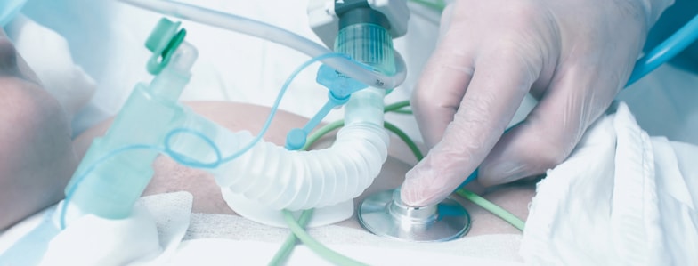 A gloved hand uses a stethoscope on an intubated patient with medical tubes in a hospital, showing medbridge healthcare training.