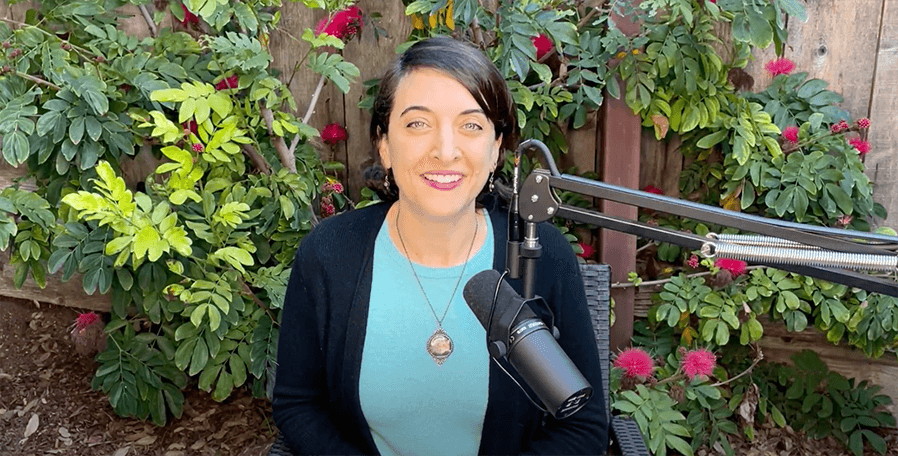 A person in a dark sweater and teal top is speaking into a microphone in a garden, possibly about healthcare training or medbridge's hybrid care solutions.