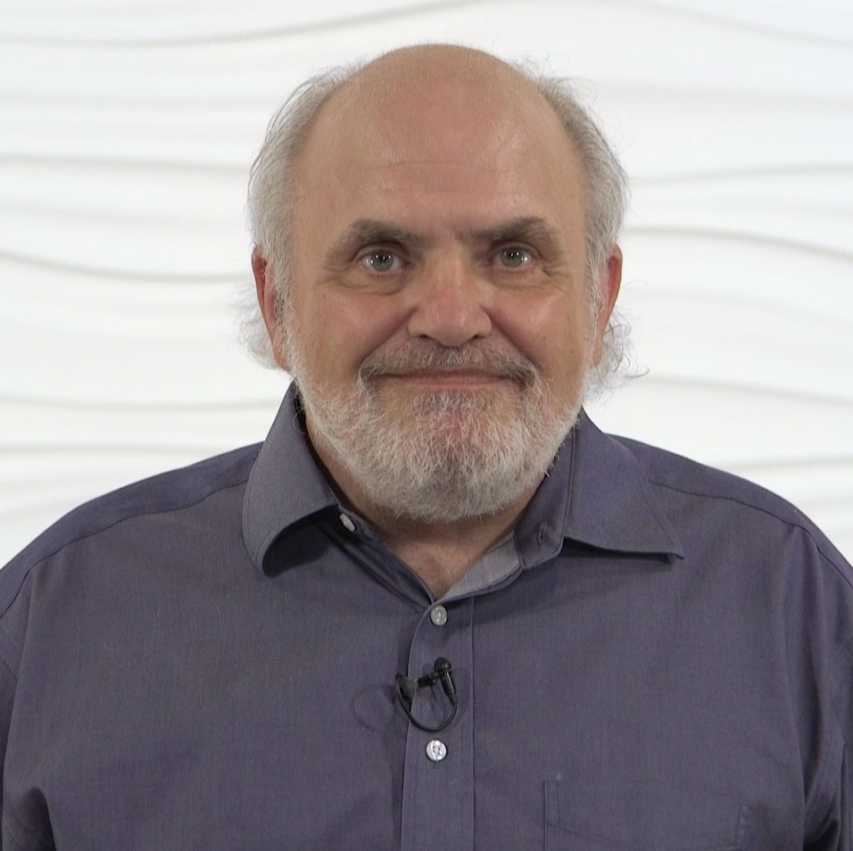 An older man with a beard, in a blue shirt and microphone, stands against a white backdrop representing medbridge's healthcare education essence.